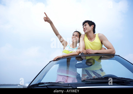 Un giovane guardando il cielo con indicando con dito in piedi sulla vettura sportiva Foto Stock
