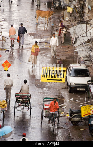 Vista dall'alto di via Paharganj a nuova Delhi, India, che mostra una scena trafficata con risciò, pedoni, una mucca e cartelli in una giornata umida. Foto Stock