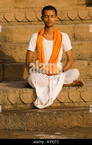 Giovane sacerdote indiano che prega e meditava in un ghat sulla riva del fiume Gange all'alba a Varanasi, Uttar Pradesh, India. Foto Stock