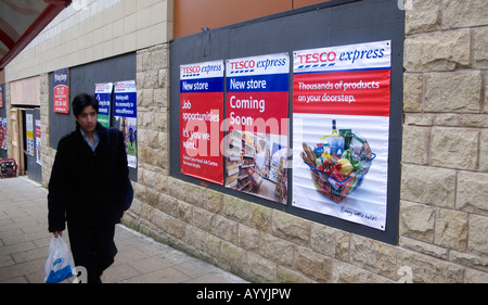 Uomo che cammina passato insegne pubblicitarie l apertura di un supermercato Tesco Express store Foto Stock