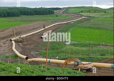 Sezioni di diametro grande trasmissione gas pipeline in acciaio infilati attraverso il paesaggio prima di essere uniti tra di loro e sepolto Foto Stock