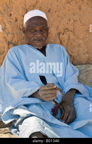 Mali, Paese Dogon. Un vecchio uomo, grani di preghiera in mano, riposa vicino alla moschea a Songho. Foto Stock