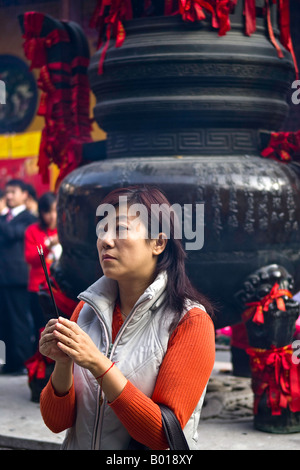 Contemporaneamente vestito giovane donna offre bruciando incenso e prega al Tempio del Buddha di Giada, Shanghai, Cina Foto Stock