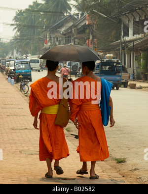 Due monaci buddisti a piedi con un ombrello attraverso la strada principale di Luang Prabang Loa Foto Stock