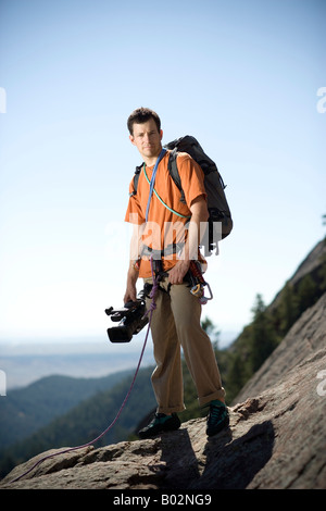 In alto su una scogliera con blue sky tutto intorno, sta un uomo con arrampicata su roccia marcia e una videocamera HD in mano. Foto Stock