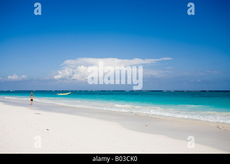 Stretching sulla spiaggia un uomo cammina lungo una spiaggia di sabbia bianca che allunga la mano verso il cielo una barca da pesca è ancorato off shore Foto Stock