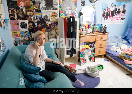 Ragazza adolescente (16 - 18) seduto sul divano del suo tipico adolescente la camera da letto di parlare sul suo telefono cellulare Foto Stock