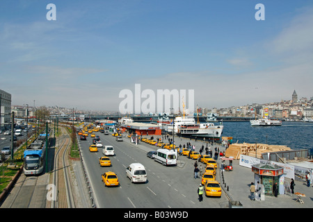 Un tram costeggia uno dei Golden Horn terminali di traghetto con il Ponte di Galata e la torre in background Istanbul Turchia Foto Stock