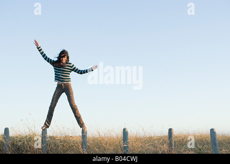 Una donna in equilibrio su pali da recinzione Foto Stock