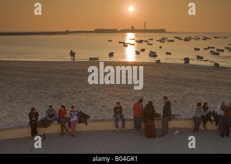 Le persone si sono riunite a Playa de la caleta al tramonto, backdropped dal Castillo de San Sebastian nella città di Cadice, Andalusia Foto Stock