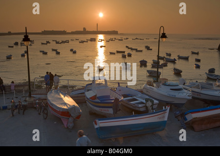 Piccole barche da pesca a Playa de la caleta backdropped dal Castillo de San Sebastian al tramonto nella città di Cadice Foto Stock