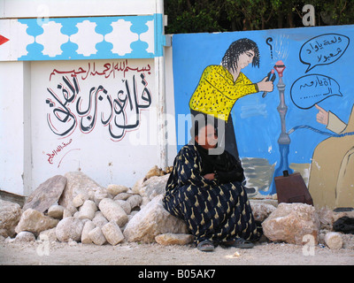 Donna anziana si rilassa sul lato della strada, parete dipinta in background, Egitto, Aswan Foto Stock