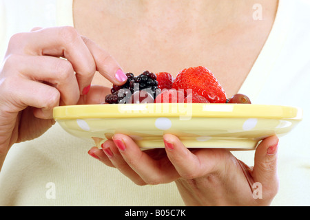 Una chiusura immagine ritagliata di un anonimo giovane donna in possesso di una piastra e di mangiare un fresco e salutare insalata di frutta da solo contro uno sfondo bianco Foto Stock