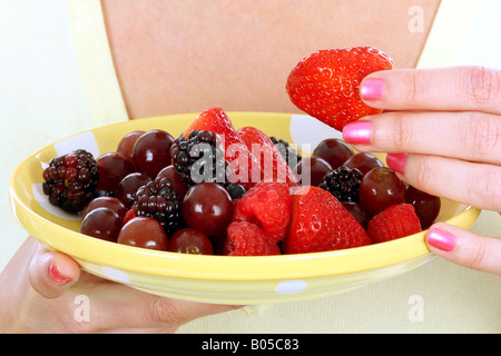 Una chiusura immagine ritagliata di un anonimo giovane donna in possesso di una piastra e di mangiare un fresco e salutare insalata di frutta da solo contro uno sfondo bianco Foto Stock