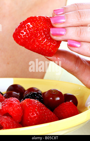 Una chiusura immagine ritagliata di un anonimo giovane donna in possesso di una piastra e di mangiare un fresco e salutare insalata di frutta da solo contro uno sfondo bianco Foto Stock