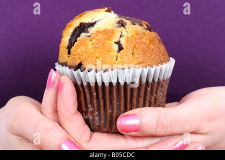 Giovane donna tenendo un fresco cotto al forno gustose Chocolate Chip Muffin torta individuale pronto a mangiare Foto Stock