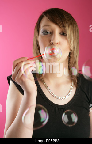 Ragazza adolescente soffiare bolle in studio contro sfondo rosa. Foto Stock