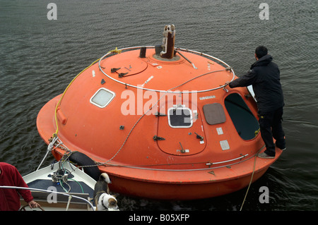 Boa arancione capsula modulo di sicurezza con l'uomo su di esso galleggiante sul fiume di acqua superficie in Den Haag, Paesi Bassi Foto Stock