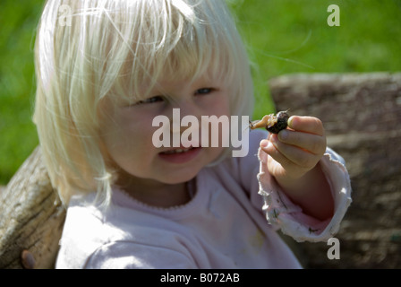 Foto di stock di una bionda dai capelli due anno vecchia ragazza esaminando una lumaca Foto Stock