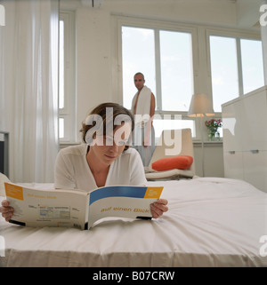 Giovane donna giaceva a letto durante la lettura di un manuale sui computer Foto Stock