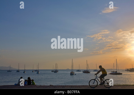 Panama, Panama City, uomo corse in bicicletta lungo la Amador Causeway al tramonto Foto Stock