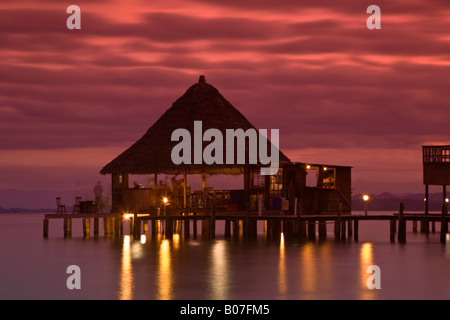 Panama, Bocas del Toro Provincia, Carenero Isola (Isla Carenero), decapato pappagallo Ristorante e bar si riflette nell'oceano al tramonto Foto Stock