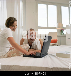 Giovane donna seduta nel letto accanto a un giovane uomo mentre si lavora con un notebook Foto Stock