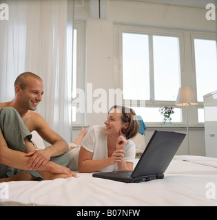 Giovane donna giaceva a letto accanto a un giovane uomo mentre si lavora con un notebook Foto Stock