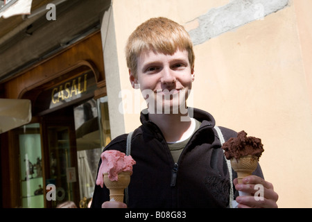 Un 14 15 anno vecchio ragazzo adolescente sorride mentre si tiene due italiani gelati al di fuori di Gelateria Casali in Lucca Italia Italy Foto Stock