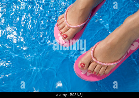 Piedi indossando flip-flop appesa sopra il lato di una piscinetta per bambini Foto Stock