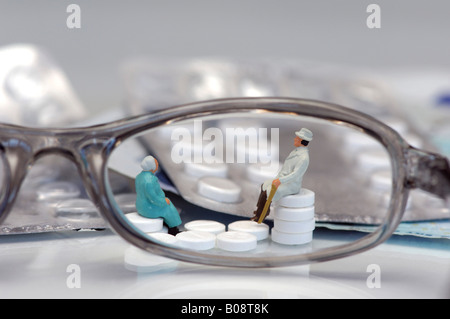 Miniatura dei cittadini anziani seduti su pile di pillole osservata attraverso un paio di occhiali Foto Stock