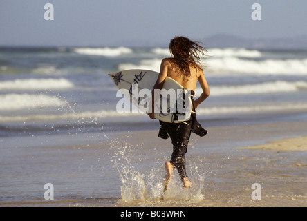 Giovani surfer che corre lungo la spiaggia con la tavola da surf sotto il suo braccio e Surfers Paradise Beach, Gold Coast, Queensland, Australia Foto Stock