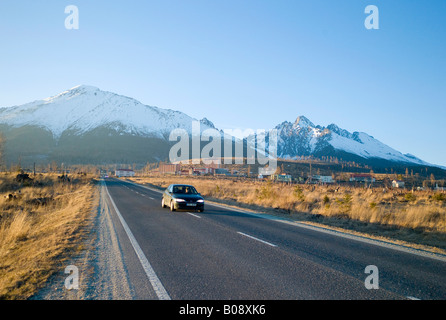 Auto guidando lungo una strada rettilinea che conduce a Tatranská Lomnica, con montagne dei Carpazi, alte cime dei Tatra (retro), vicino Vysoké Foto Stock