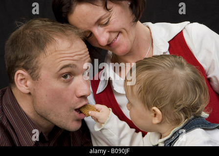 I genitori con la figlia, bambino alimentando il suo papà con un cookie Foto Stock