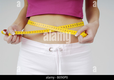 Giovane donna per misurare le dimensioni della sua vita con una cintura a nastro di misurazione Foto Stock