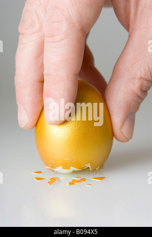 Uovo di Colombo, posizionamento mano golden egg sul suo fondo incrinato Foto Stock