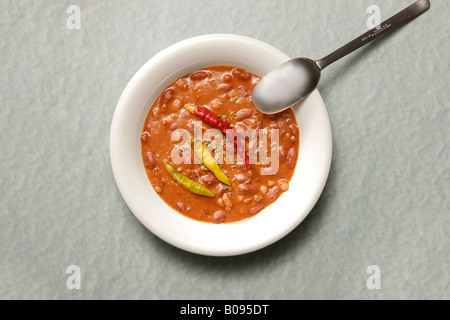 Cucchiaio a fianco di chili con carne guarnita con peperoncino su una piastra bianca Foto Stock