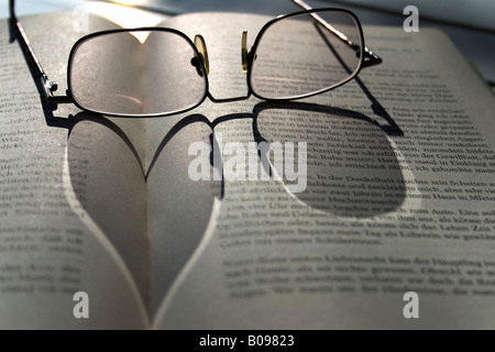 A forma di cuore ombra di un paio di occhiali che giace su di un libro Foto Stock