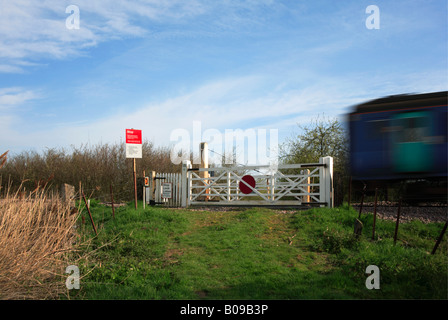 Passaggio a livello e cancello pedonale sul Norwich per Great Yarmouth linea ferroviaria con cartelli di avvertimento e passando il treno. Foto Stock