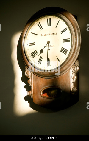 Vecchia caduta in legno quadrante di orologio a pendolo realizzato in Pwllheli in una patch di luce del sole sulla parete di una cappella nel Galles del nord Foto Stock