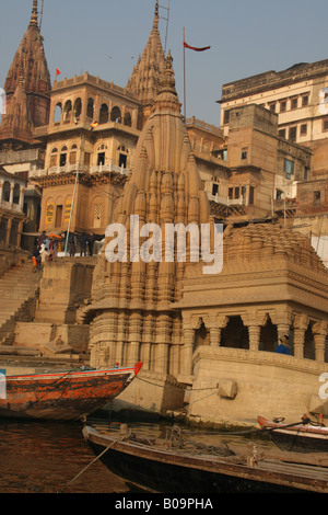 Un rosso e blu dipinto di imbarcazione attraccata vicino a un pendente tempio di Shiva in Varanasi Foto Stock