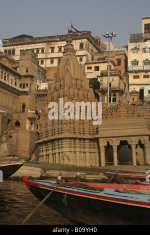 Un rosso e blu dipinto di imbarcazione attraccata vicino a un pendente tempio di Shiva in Varanasi Foto Stock