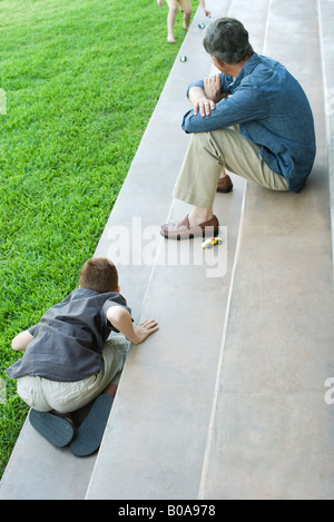 Nonno e nipoti seduti sui gradini di giocare con le macchinine, ad alto angolo di visione Foto Stock