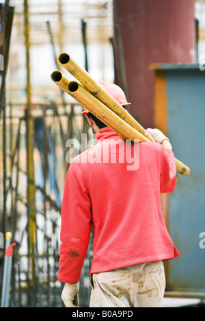 Lavoratore presso il sito di costruzione portando le aste metalliche sulla spalla Foto Stock