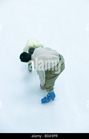 Padre e figlio pattinaggio sul ghiaccio insieme, sia di piegarsi, ad alto angolo di visione Foto Stock