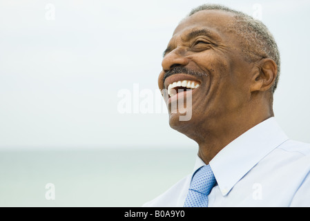 Imprenditore Senior ridendo, mare sullo sfondo, la testa e le spalle Foto Stock