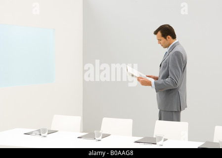 Imprenditore in piedi accanto al tavolo da conferenza, giornale di lettura Foto Stock