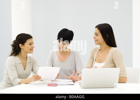 Tre professionisti femmina seduta a tavola, avendo discussioni, un documento di contenimento Foto Stock