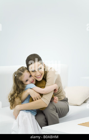 Giovane madre abbraccia bambina, sorridente in telecamera Foto Stock