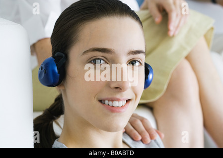 Ragazza adolescente ascoltando le cuffie, sorridente alla fotocamera, donna di mano sulla sua spalla Foto Stock